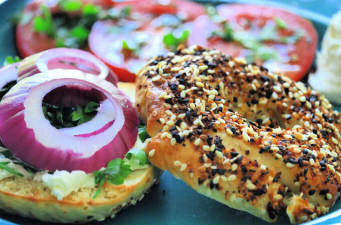 close up photo of an everything bagel with avocado and sliced onion