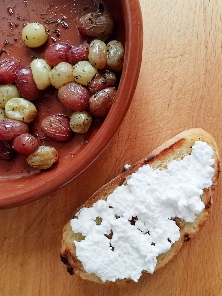toast spread with ricotta cheese next to a bowl of roasted grapes