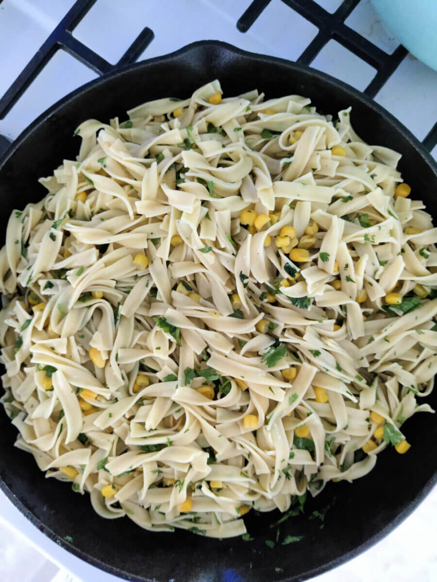 buttery noodles with herbs and corn in a skillet